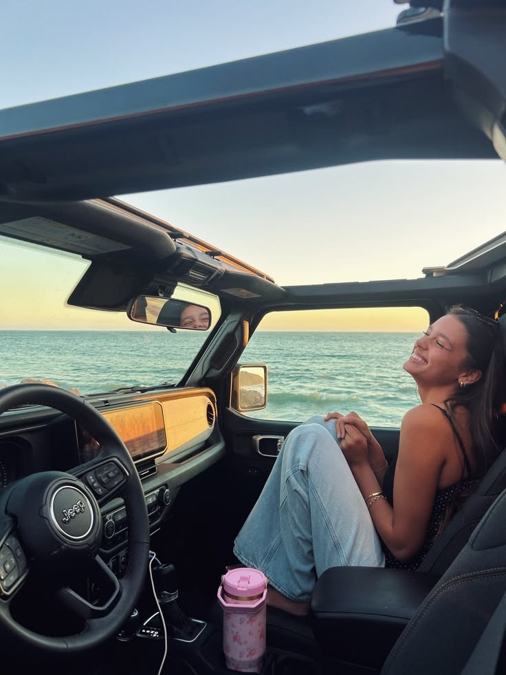 Passenger smiling in a Jeep parked by the ocean at sunset